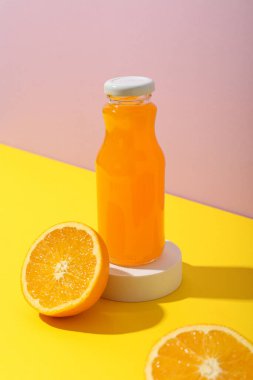 Pembe arka planda meyve suyu ve portakallı cam şişe.