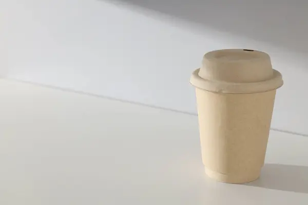 A paper cup with a lid on a light background