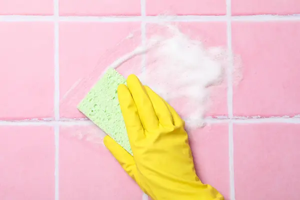 Washing pink tiles in rubber gloves close-up