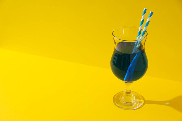 Blue cocktail with straws in glass on yellow background, space for text