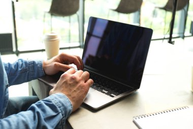 Bilgisayarda çalışan adam, kahve fincanı ve defterler çalışma alanındaki masada, kapat.
