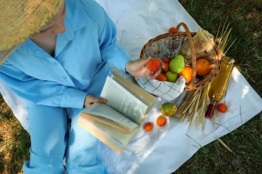 Hasır şapkalı bir kız piknik kitabı okuyor.