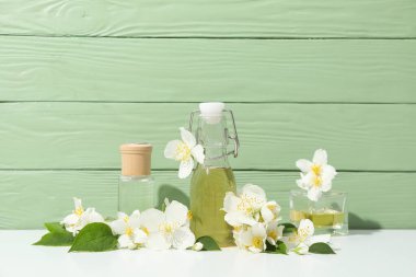 Yeşil ahşap arka planda yasemin çiçekleri ve parfüm şişeleri