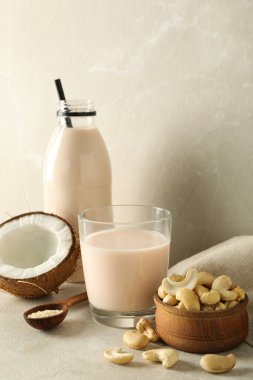 Alternatif süt, hindistan cevizi ve fındıklı bej arka planda bardak ve şişe.