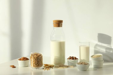 Alternatif sütle dolu şişe ve bardak ve hafif arka plandaki kaselerde bitkisel malzemeler