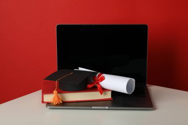 Diplomalı şapka, kırmızı arka planda kitap ve dizüstü bilgisayar..