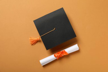Mezuniyet şapkası ve turuncu arka plan diploması..