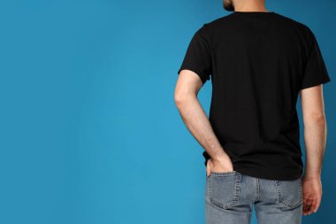 Mavi arka planda siyah tişörtlü genç bir adam.