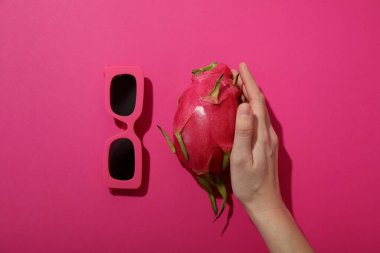 Elde ejderha meyvesi ve pembe arka planda güneş gözlüğü.