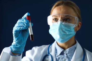 Elinde donör kanı olan ve mavi arka planda test tüpü olan kadın doktor.