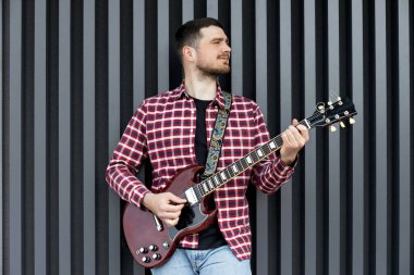 Kaliteli bir genç adam koyu bir arka planda gitar çalar.