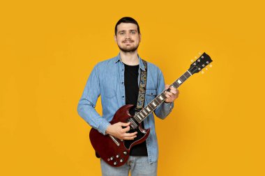 Elinde sarı bir arka planda gitar olan çekici bir genç.