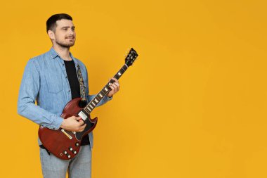 Elinde sarı bir arka planda gitar olan çekici bir genç.