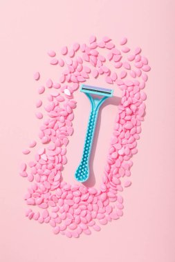 Tüy dökümü için balmumu tanecikleri ve pembe arka planda bir tıraş bıçağı.