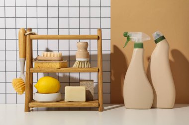 Fırçalar, sünger, sabun, ahşap rafta limon ve arka planda deterjan şişeleri
