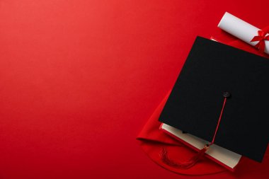 Kırmızı arka planda diploması olan mezun şapkası..