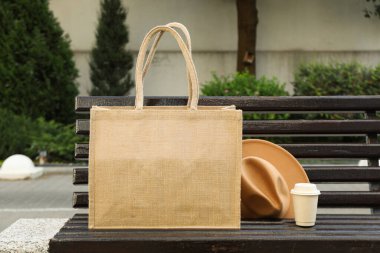 A bag with coffee and a hat on a bench