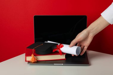 Diplomalı şapka, kırmızı arka planda kitap ve dizüstü bilgisayar..