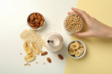 Bir şişe süt, bitkisel malzemeler ve arka planda el, üst manzara.