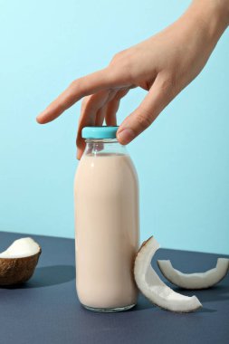Mavi arka planda bir şişe süt, el ve hindistan cevizi.