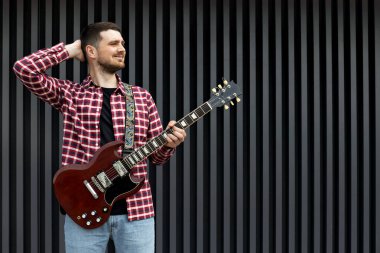 Kaliteli bir genç adam koyu bir arka planda gitar çalar.