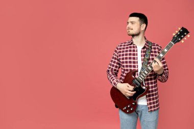 Pembe arka planda gitar çalan çekici bir genç adam.