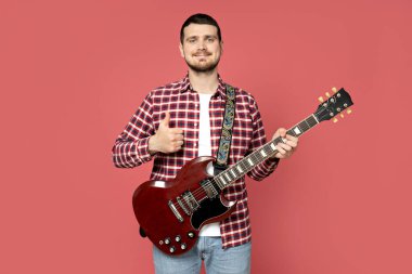 Pembe arka planda gitar çalan çekici bir genç adam.