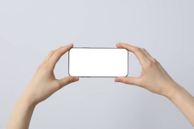 Gri arka planda akıllı telefon tutan kadın eller.