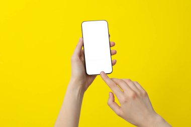 Sarı arka planda akıllı telefon tutan bir kadın.