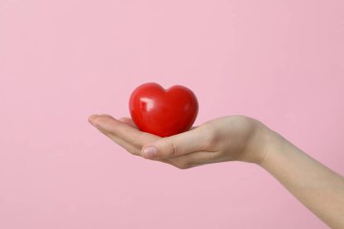 Bir kadın eli kırmızı bir kalbi tutar.