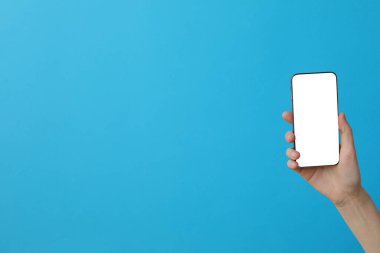 Mavi arka planda akıllı telefon tutan bir kadın.