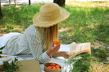 Hasır şapkalı bir kız piknik kitabı okuyor.