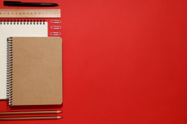 Kırmızı zemin üzerinde kırtasiye malzemesi olan iki defter.