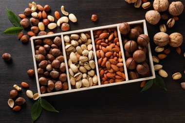 Wooden box with different nuts on a dark background clipart