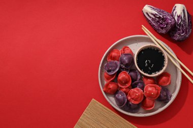 Tabakta renkli hamur köftesi, soya sosu, yemek çubukları ve kırmızı arka planda lahana parçaları, metin için yer