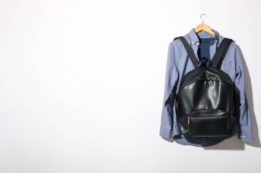 Beyaz arkaplanda askıya asılı tişört, gömlek ve sırt çantası, metin için boşluk