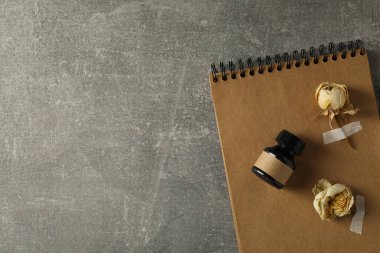 Kurumuş beyaz gül tomurcukları, not defteri ve gri arka planda bir şişe mürekkep, metin için boşluk