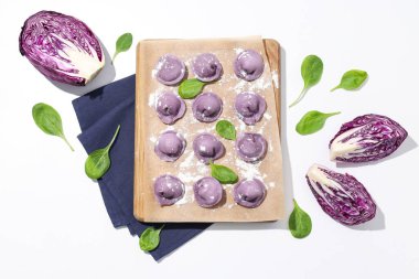 Mutfak tahtasında mor hamur tatlısı, beyaz arka planda fesleğen ve lahana.