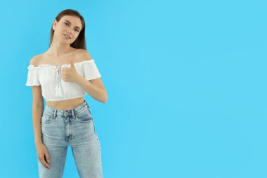 Mavi arka plandaki çekici genç kız başparmağını kaldırıyor.