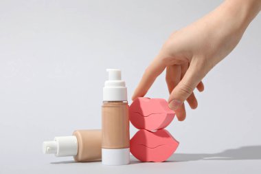 Temeli olan şişeler, beyaz arka planda kadın eli ve kozmetik süngerler.