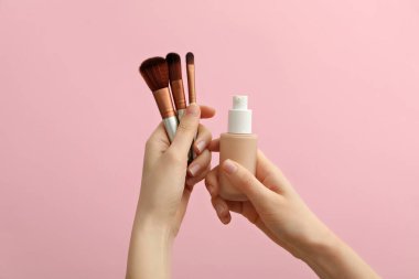 Temelli fırçalar ve şişeler pembe arka planda kadın ellerinde
