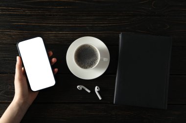 Kulaklıklı bir fincan kahve, bir defter ve arka planda bir akıllı telefon.