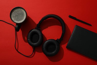 Kulaklıklı siyah bir fincan çay ve kırmızı arka planda bir defter.