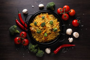 Kızartma tavasında pilav ve koyu ahşap arka planda sebzeler.