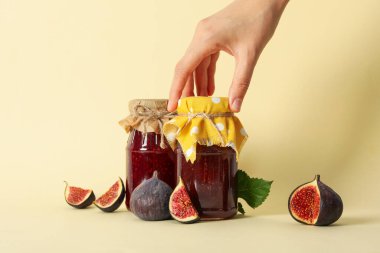 İncir, reçel kavanozları ve bej arka planda el.