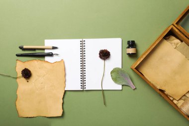 Yeşil arka planda çiçek, kutu, not defteri ve kalem, üst görünüm.