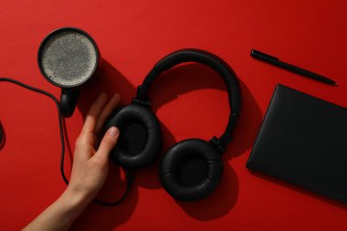 Kulaklıklı siyah bir fincan çay ve kırmızı arka planda bir defter.