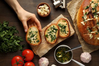 Sarımsaklı ekmek, domates, maydanoz, tereyağı ve el ahşap arka planda, üst manzara