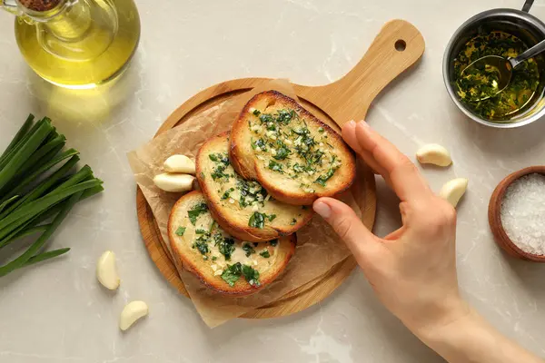 Gemide sarımsaklı ekmek dilimleri, malzemeler ve bej arka planda el, üst manzara.