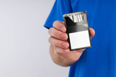 Mavi tişörtlü bir adamın elinde bir paket sigara.